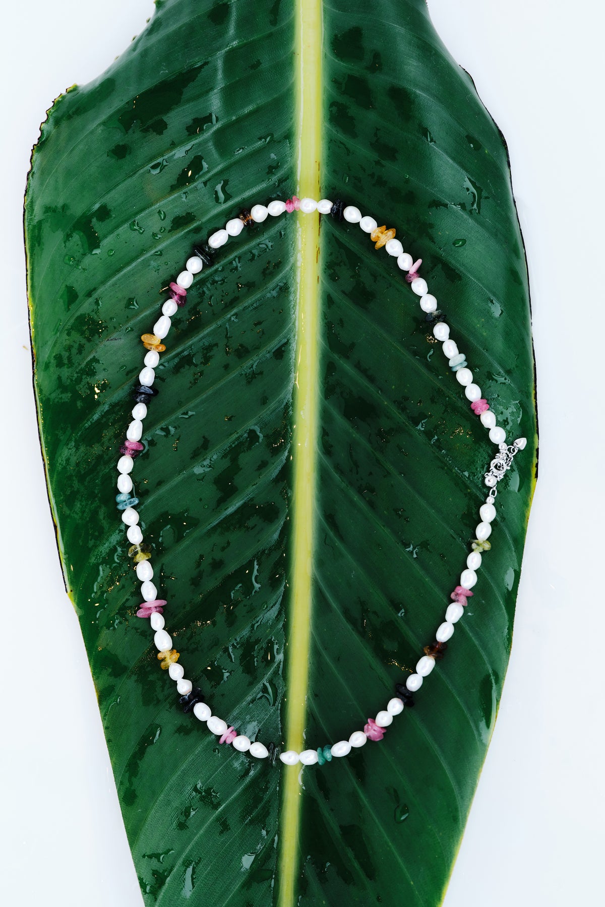 Electric Shore pearl and multicolor tourmaline necklace arranged on a wet tropical leaf