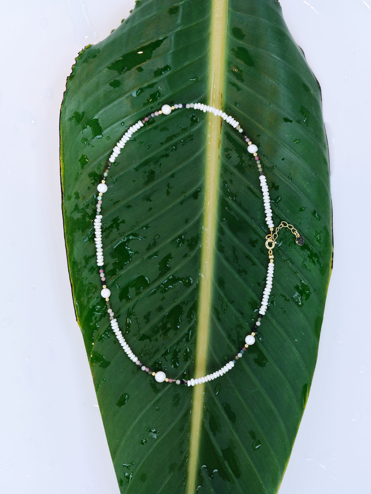 Midnight Pearl Current Necklace with pale pearls and scattered dark accents on a green leaf