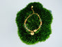 Golden Ingot Current Bracelet with clear crystal beads and a 24K gold-plated copper yuanbao charm on green moss.