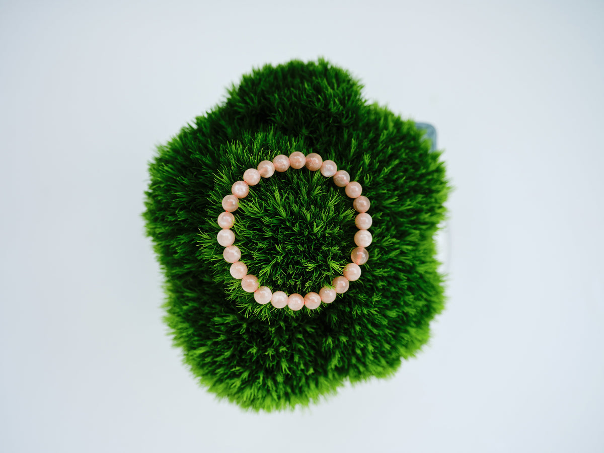 Golden Hour Bracelet with warm peach sunstone beads arranged in a circle on deep green moss