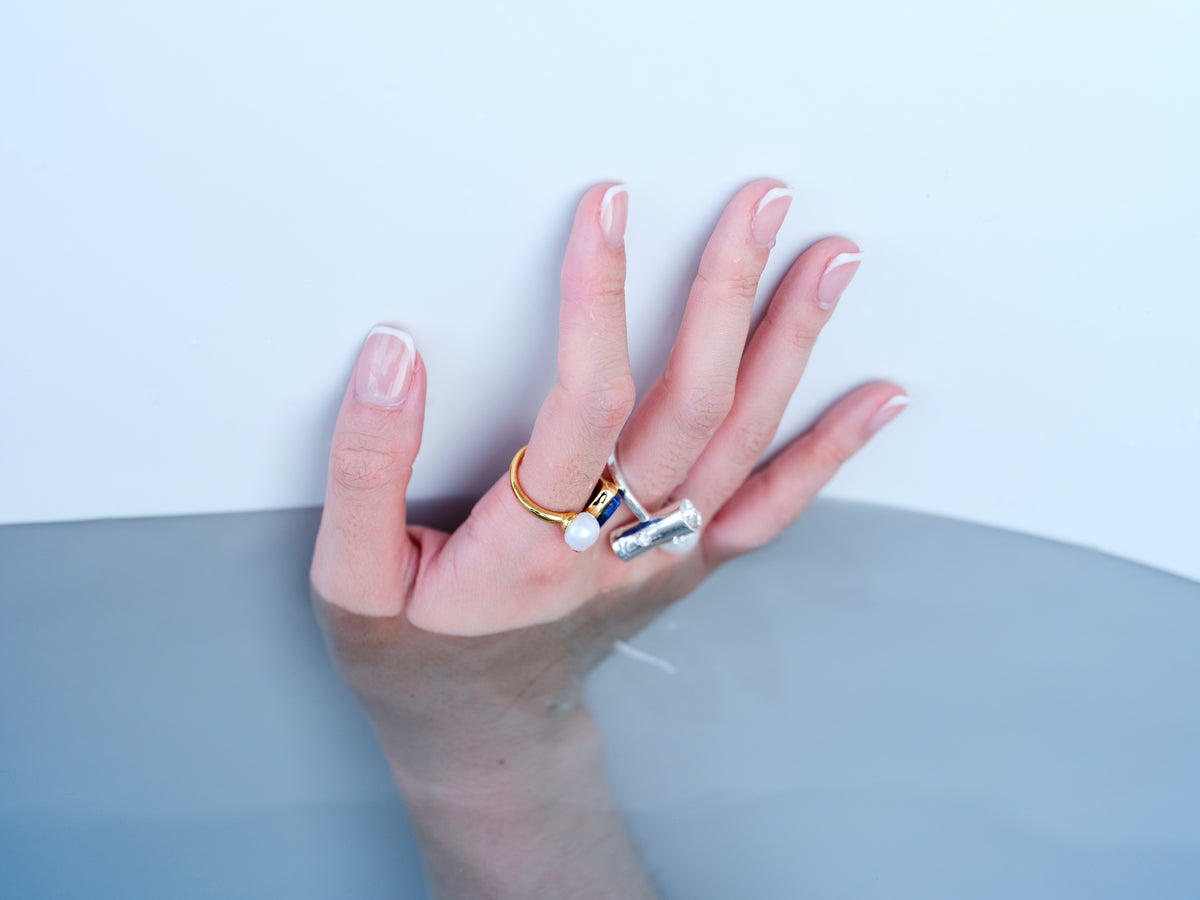 Adjustable pearl and gemstone rings styled on a hand against a pale blue water setting